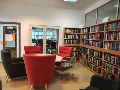 Nowy kącik beletrystyczny w Bibliotece Ekonomicznej. Na zdjęciu są regały z książkami, wokół wysokie fotele i lampa. 