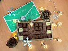 Na zdjęciu kompozycja świąteczna: czekolada w formie życzeń, szyszki i świecące  