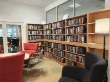 Nowy kącik beletrystyczny w Bibliotece Ekonomicznej. Na zdjęciu są regały z książkami, wokół wysokie fotele i lampa. 