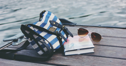 Płucienna torba, książka i okulary leżące na drewnianym pomości, w tle woda